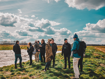 Adults standing in a group talking in a field, blue skies with clouds above