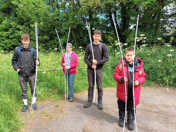 Four young people stand holding white poles in front of long grass and trees
