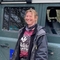 Nicky, wearing a Wildlife Trusts Tshirt, jacket and scarf, stands smiling next to a vehicle