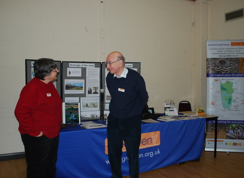 Lady and Man stand in front of a table with a display board of Great Fen information 