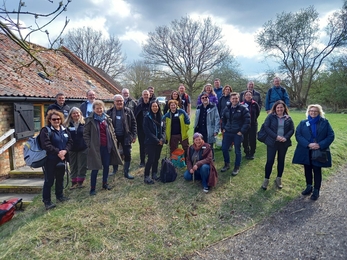 Crowd of people smiling to camera, stood on grass mound in front of old brick building