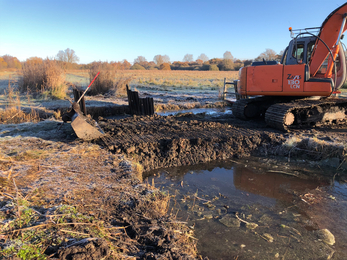 Digger creating mud culvert bridge in water