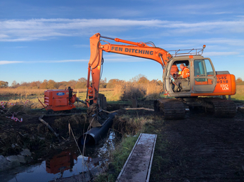 Digger creating mud culvert bridge in water