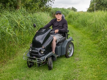 A man sits on an all-terrain mobility scooter in a nature reserve