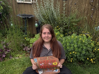 Kaitlyn sits in her garden holding a hand-drawn roof tile with three more around her
