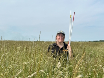 Kaitlyn stands in tall grass holding quadrat poles