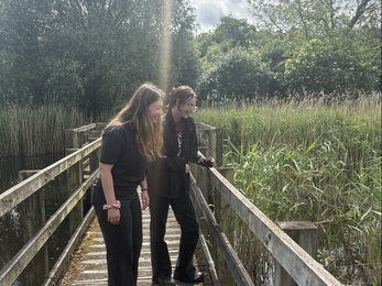 Natalie and Lucy look over the bridge into a pond on a sunny day