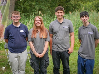 Three young boys and one young girl standing in a line wearing Wildlife Trust outfits, smiling at the camera