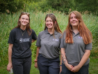 Three young woman dressed in Wildlife Trust tops standing side by side smiling at the camera