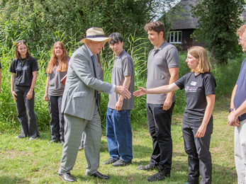 A line of young people with a Wildlife Trust work clothes. The Duke of Gloucester is reaching out to shake a hand of a young woman