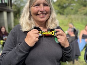 Catherine stands outside the Rothschild Bungalow showing a badge made of Lego that says Peat Restoration Minion