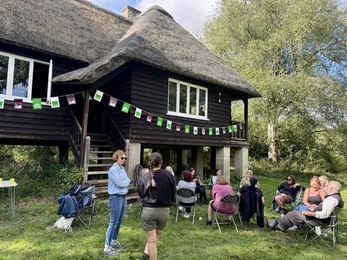 People sat on chairs and standing in sunshine outside Rothschild Bungalow at Woodwalton Fen