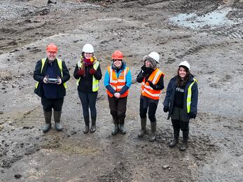 Group of 5 people in high vis and hard hats smiling up at the drone camera