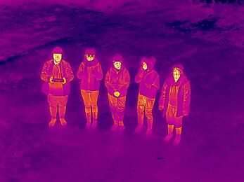 Group of 5 people in high vis and hard hats smiling up at the drone in infra-red