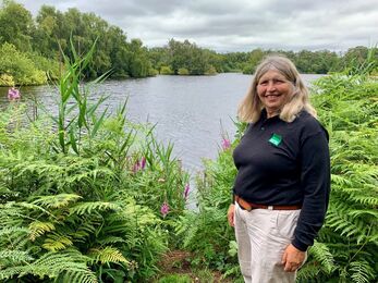 Catherine stands in front of a lake in Natural England branded top