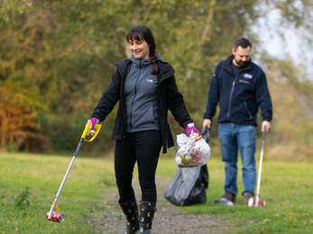 Lady walking in front and man behind in green park with litter pickers and rubbish bags