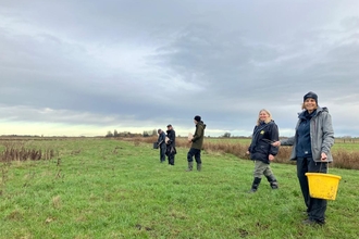 Adults stand in a line on a field spreading seed by hand. 