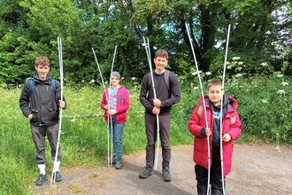 Four young people stand holding white poles in front of long grass and trees