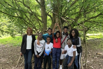 A group of black adults and children stand beneath a tree smiling to camera