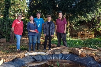 Three adults and two teenagers stand by a newly built pond