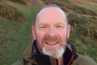 Adam takes a selfie standing on green hillside