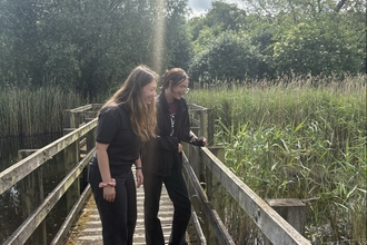 Natalie and Lucy look over the bridge into a pond on a sunny day