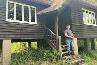 Sam stands on the steps to the Rothschild Bungalow, holding binoculars