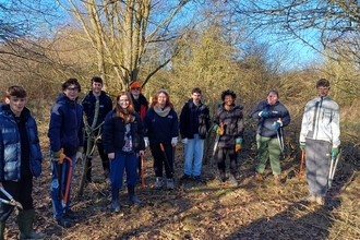 A group of young people stand in woodlands on a sunny winter day with various tools such as saws and loppers