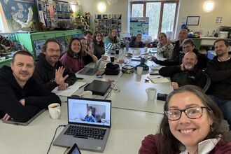 Large group of staff sat around tables for meeting, taking selfie