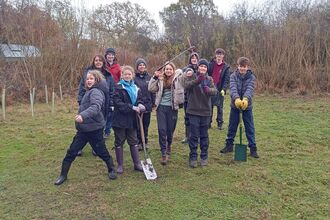8 young people stand with two staff members, all wearing winter coats, boots, gloves and a few holding gardening tools