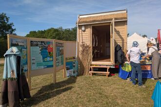 Wooden tiny house with unfolded information boards and a handmade cloak on display