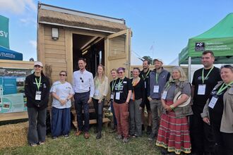 A group of people stand outside a wooden tiny house at a trade show