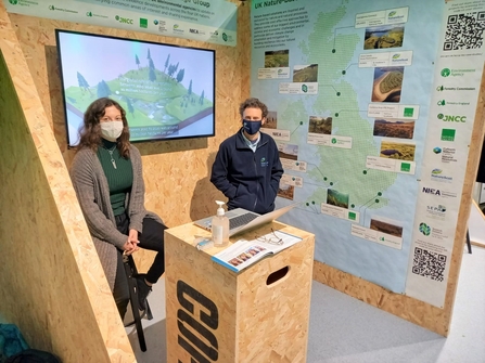 Two adults sat in front of a screen mounted on wooden wall
