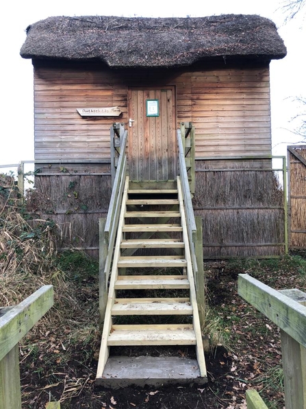 Newly replaced wooden steps leading up to a wooden hide with thatched roof