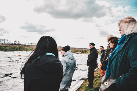 group of adults standing looking over field with white steam weeding mat laid out