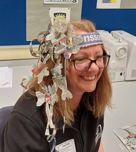 Rebecca sits smiling wearing a paper headband decorated with newspaper butterflies and flowers