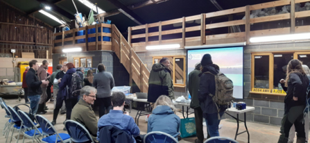 Group of adults sitting and standing in a barn ready for a presentation on a pull down screen