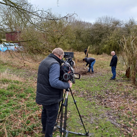 A cameraman focuses a camera on Lewis working in the garden