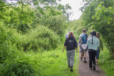 Group of young people and a Wildlife Trust staff member walk away from camera through a nature reserve