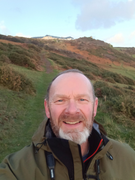 Adam takes a selfie standing on green hillside
