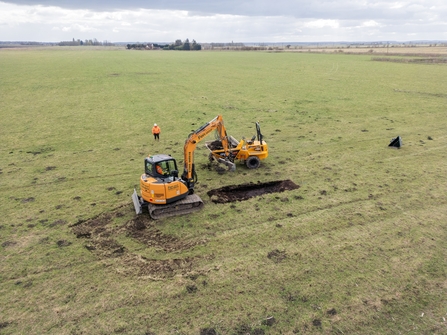 A drone shot of a digger cutting a channel into a grassed field