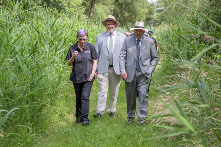 Lorna Parker, Brian Eversham and the Duke of Gloucester walk through green Woodwalton Fen nature reserve on a sunny day