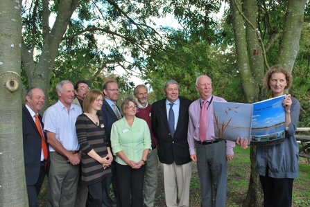 A group of adults stand under trees looking at a large A2 copy of the Great Fen Masterplan