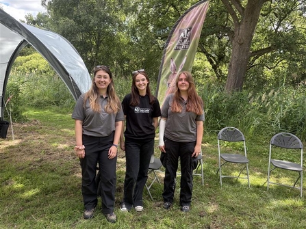 Three young woman dressed in Wildlife Trust tops standing side by side smiling at the camera