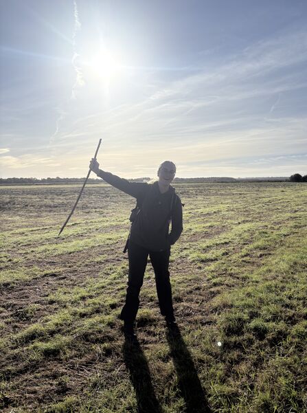 Katie stands in a field holding a stick