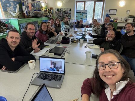 Large group of staff sat around tables for meeting, taking selfie