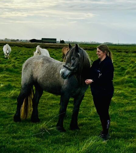 Kate stands stroking a grey pony