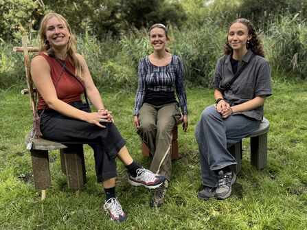Three ladies sit on handmade chairs in a nature reserve