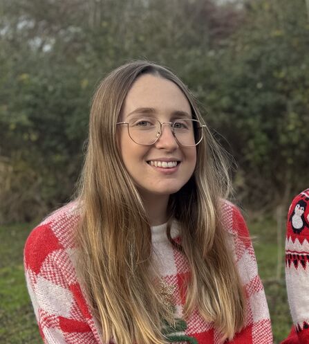 Ellen sits outdoors wearing a Christmas jumper smiling to camera