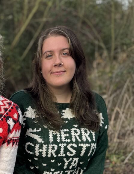 Kaitlyn sites outdoors wearing a Christmas jumper smiling to camera